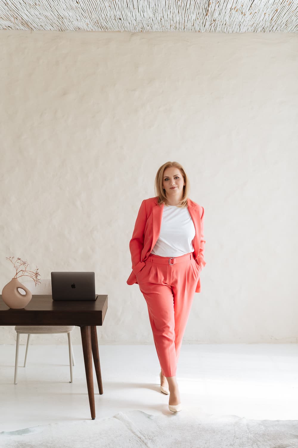Viki, host of Where She Leads, standing in a coral suit beside a desk